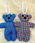Two teddy bear ornaments, one blue and one plaid, on a fluffy white background.