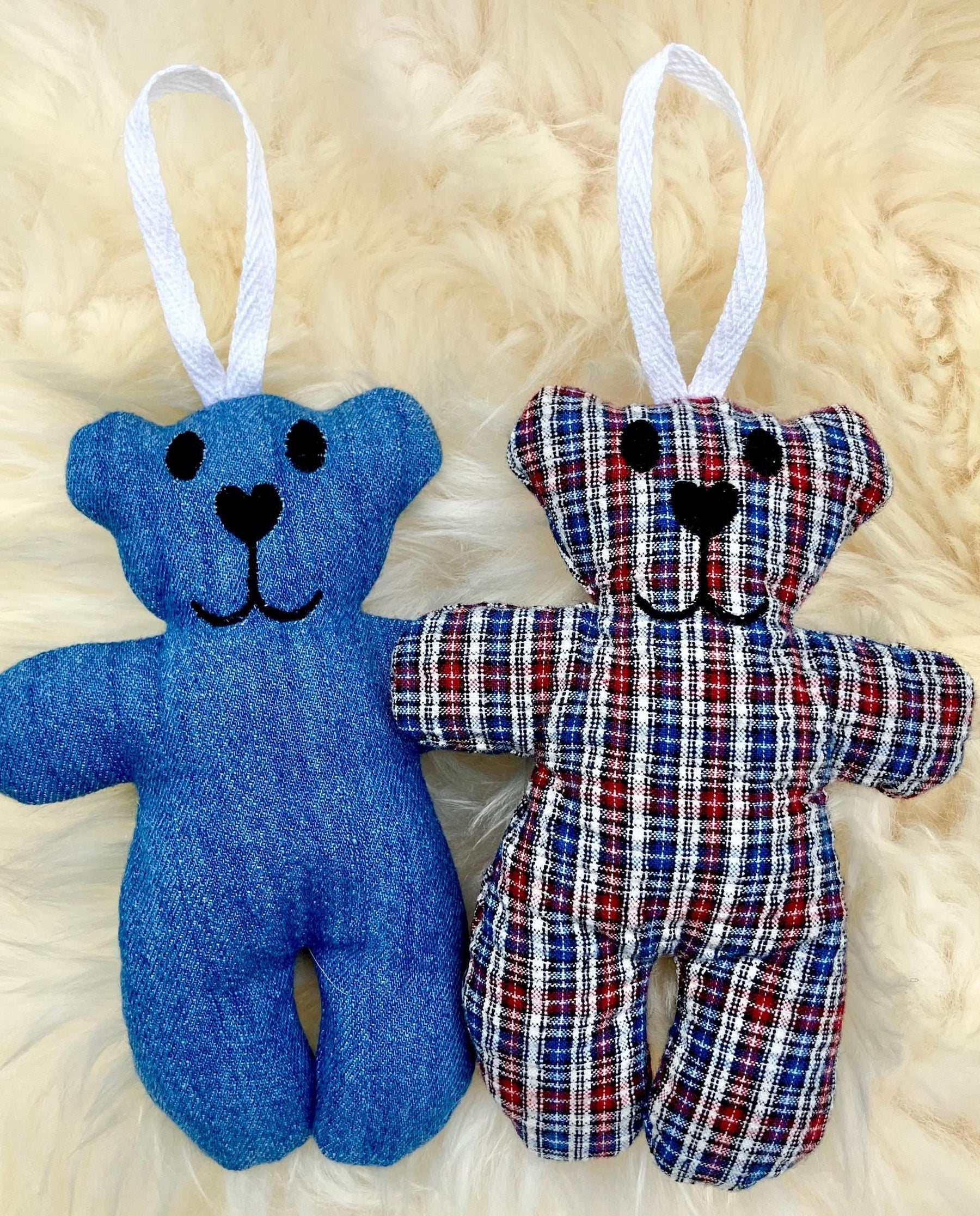 Two teddy bear ornaments, one blue and one plaid, on a fluffy white background.