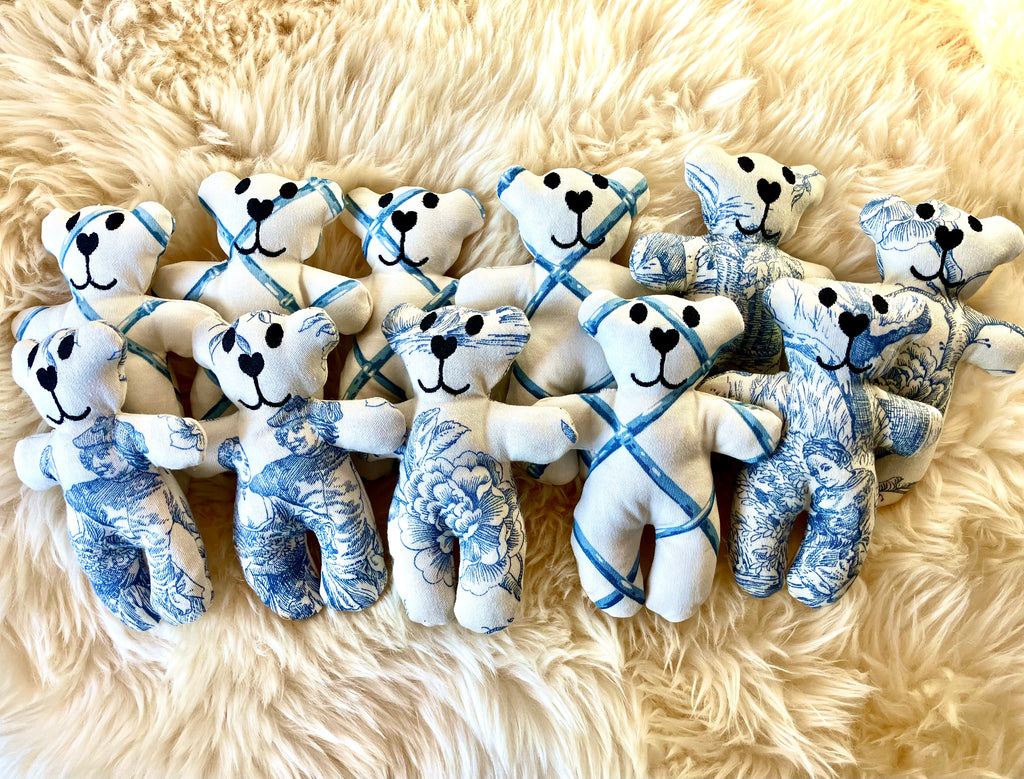 Plush teddy bears with blue and white patterns arranged on a fluffy beige surface