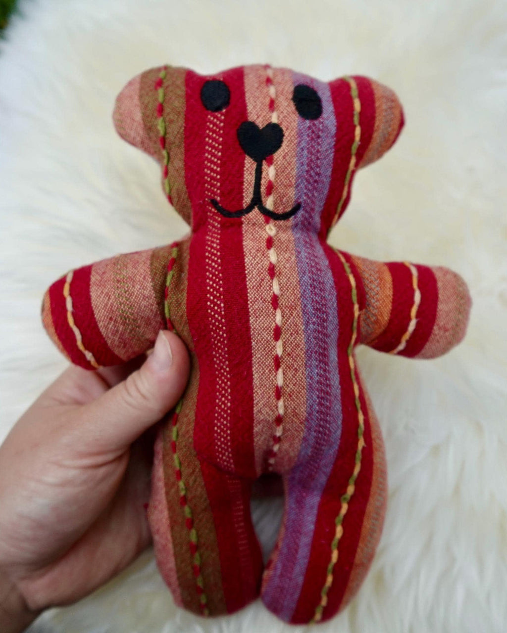 Hand holding a small striped teddy bear against a fluffy white background