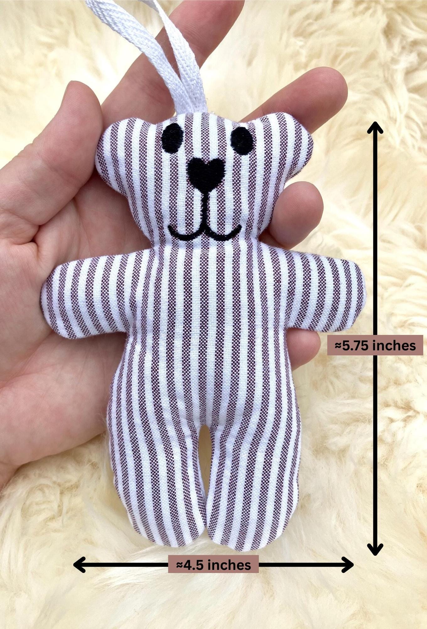 Small striped toy bear held in a hand with measurements indicated