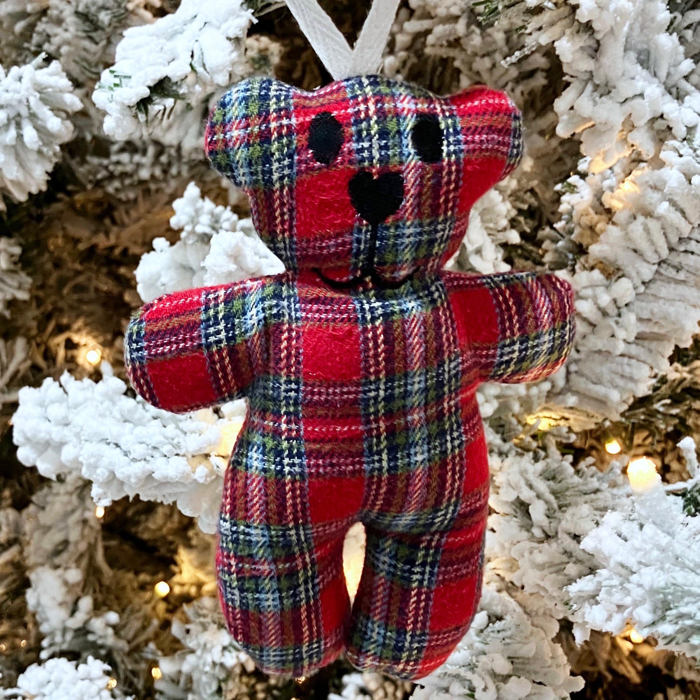 Red plaid teddy bear ornament on a decorated Christmas tree.