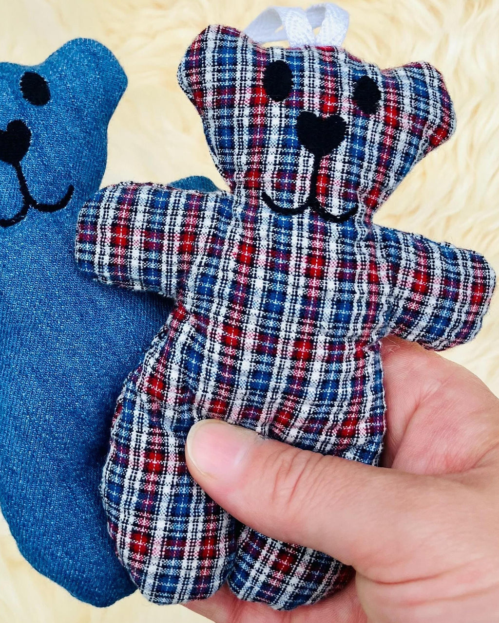 Two small teddy bears, one blue and one plaid, held against a textured yellow background.